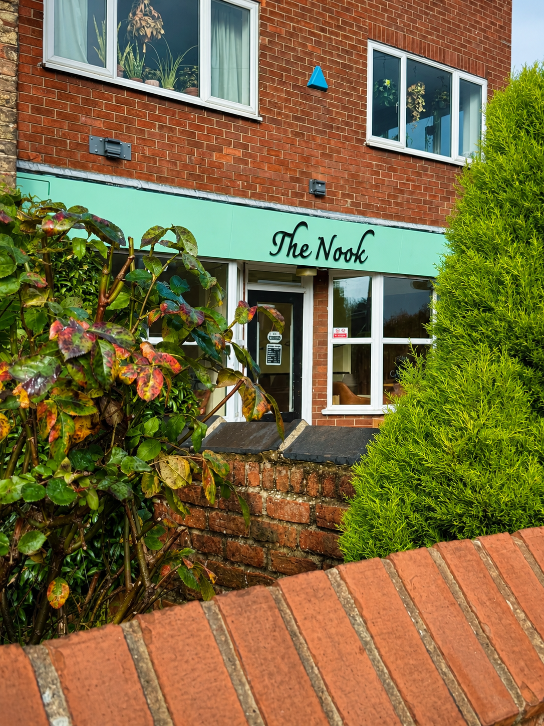 The Nook Cafe storefront framed by garden greenery in Woodthorpe